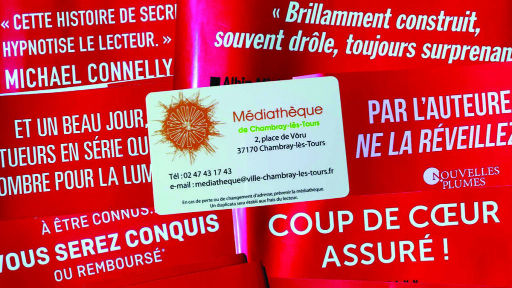 bandeaux rouges de critique de livre, et carte d’abonné de la Médiathèque au centre.